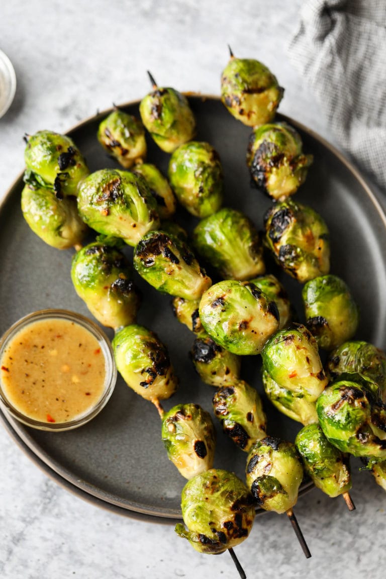 Overhead view of a plate of grilled brussels sprouts on skewers topped with a maple mustard glaze. 