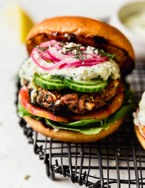 A grilled turkey burger in a bun with lettuce, tomato, tzatziki sauce, and pickled onions