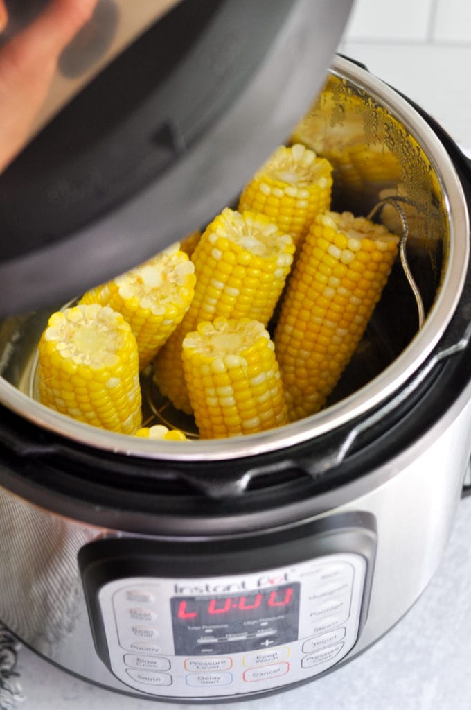 The lid of an Instant Pot being lifted off to reveal cooked corn on the cob