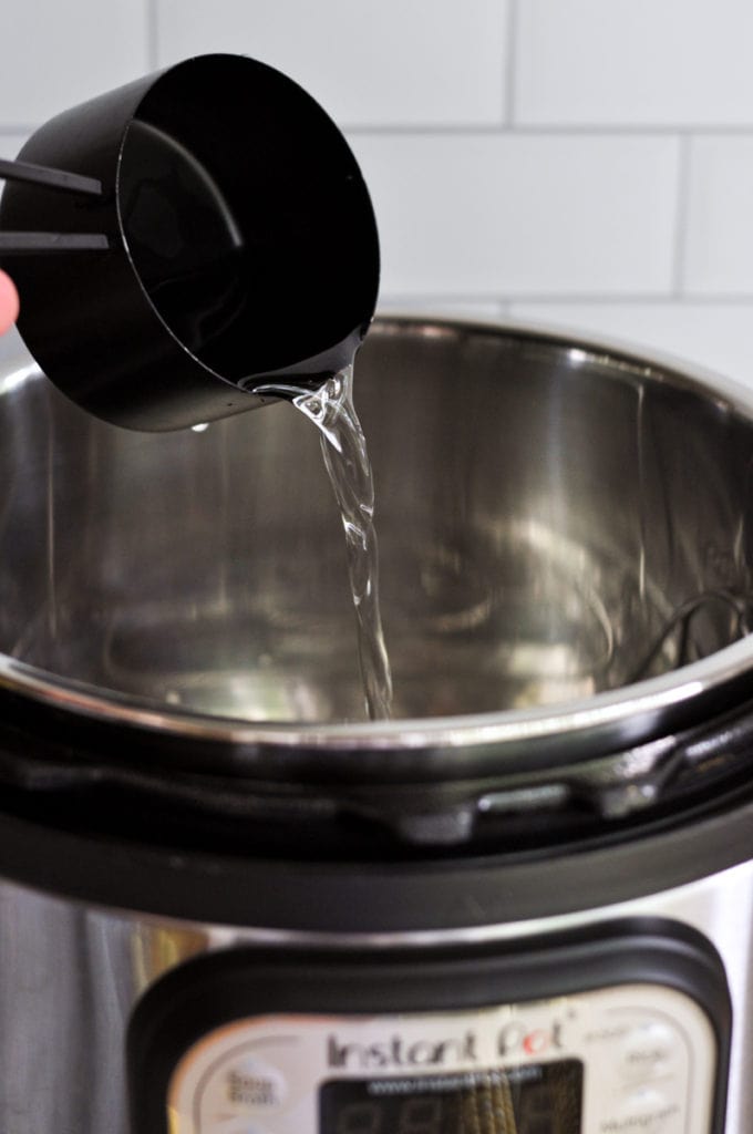 A cup of water being poured into an Instant Pot from a black measuring cup