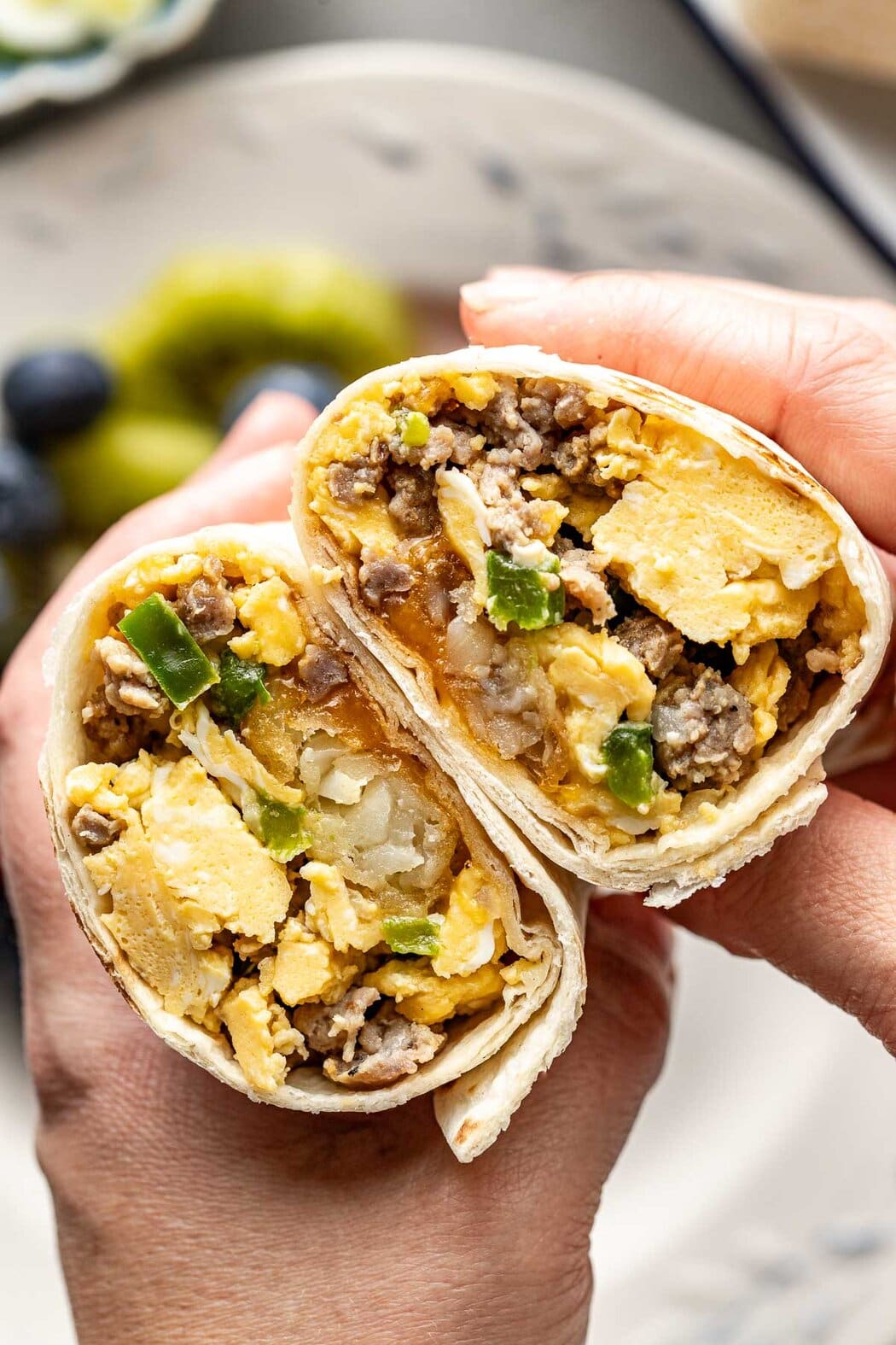 Close up view of hands holding a breakfast burrito cut in half showing the texture and ingredients of the egg and sausage mixture on the inside. 