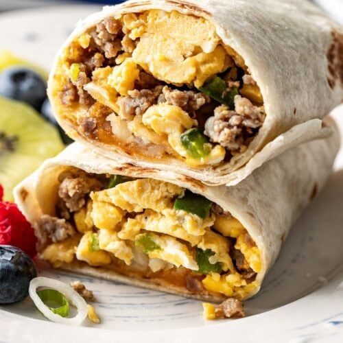 Close up view of a plate filled with a breakfast burrito cut in half showing the egg and sausage mixture on the inside with fruit on the side.