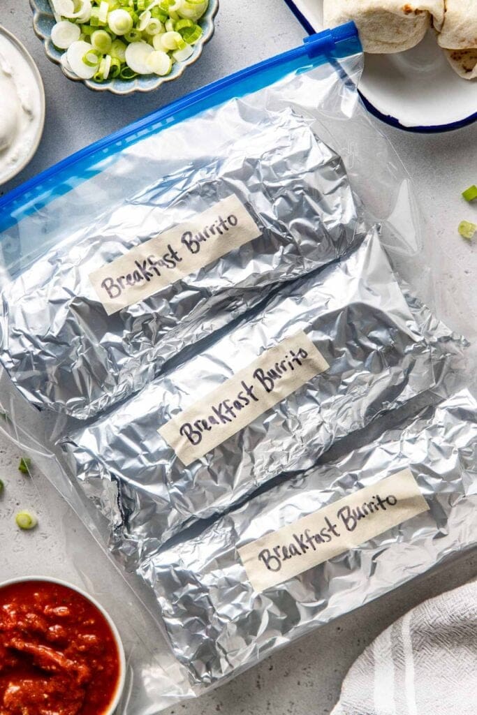 Overhead view of a zip lock bag filled with foiled wrapped Meal Prep Breakfast Burritos and labeled with tape saying breakfast burritos.