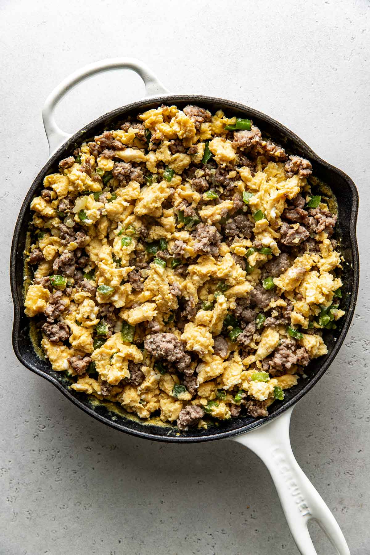 Overhead view of a skillet filled with scrambled eggs, ground sausage and green peppers. 