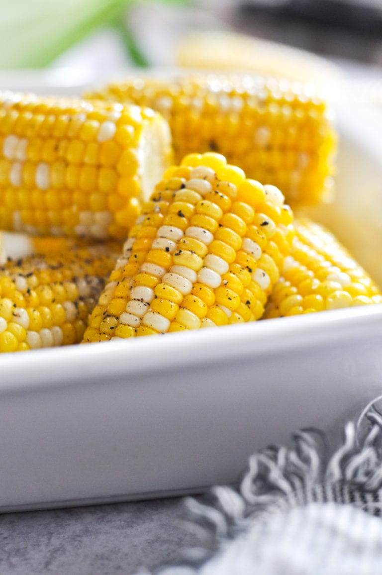 Corn on the cob made in the Instant Pot in a white serving dish with cracked black pepper sprinkled on top