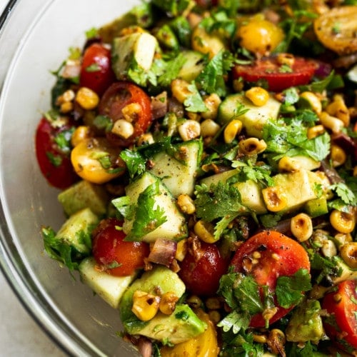 A close up of corn and avocado salad topped with cilantro and cherry tomatoes in a mixing bowl