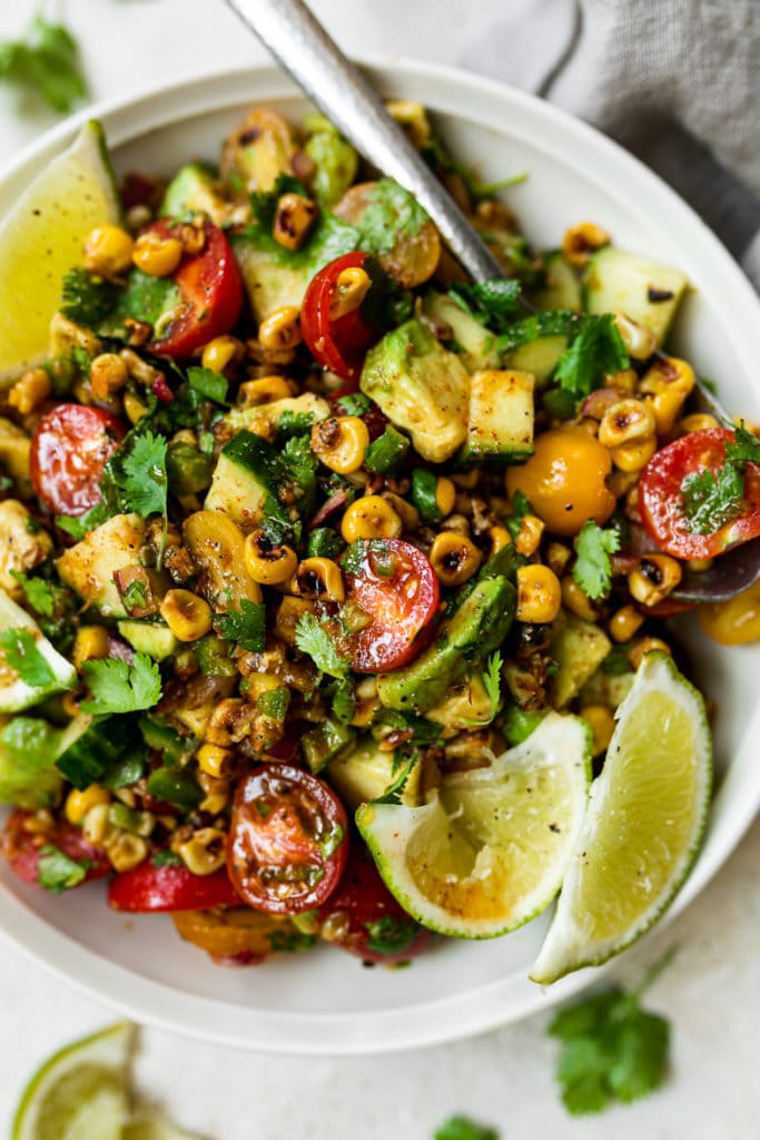 Roasted corn salad with cherry tomatoes, cucumbers, avocado, and cilantro tossed in chili lime dressing and served on a white plate