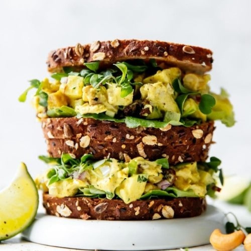 Two overfilled curry chicken salad sandwiches stacked on top of each other on a white plate