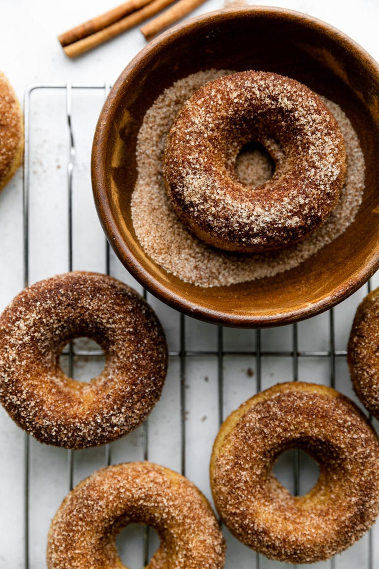 Cinnamon sugar baked donuts on a wire rack, one in a bowl of cinnamon sugar.