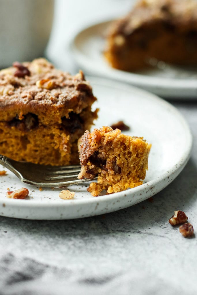 A fork full of fluffy and moist gluten-free pumpkin coffee cake on a speckled plate. 