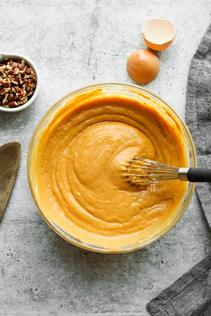 Pumpkin coffee cake batter in a clear mixing bowl with whisk in batter