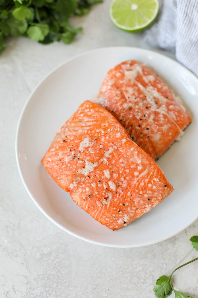 Two salmon fillets perfectly grilled laying on a white plate.