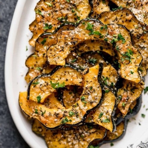 Herb and parmesan crusted acorn squash pieces on a white serving tray.