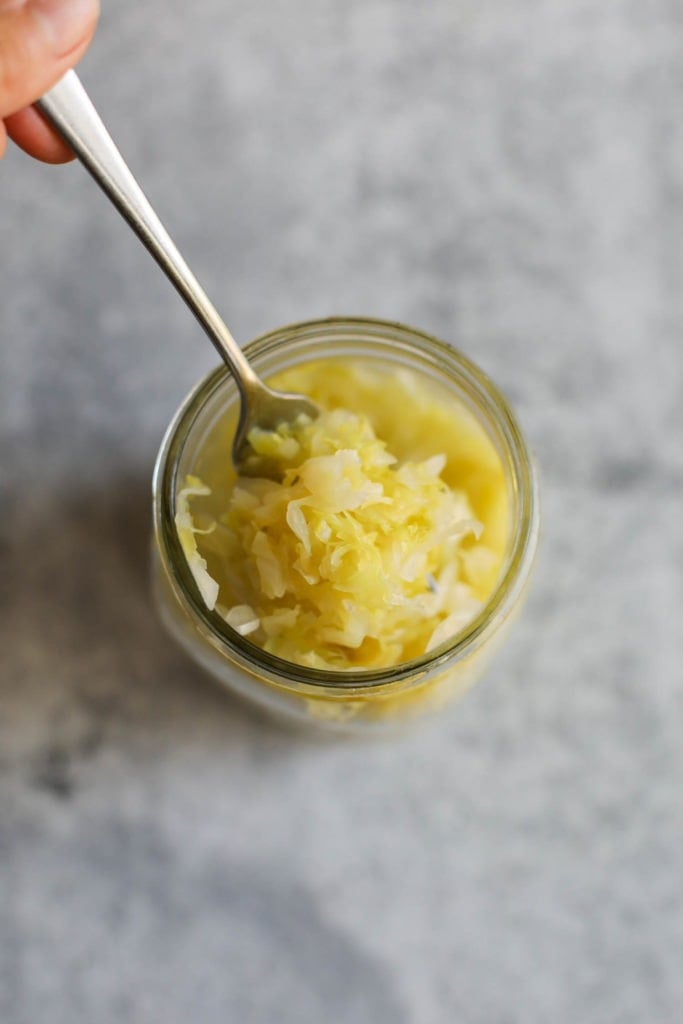 Overhead view of homemade sauerkraut in a mason jar being scooped out with a fork. 