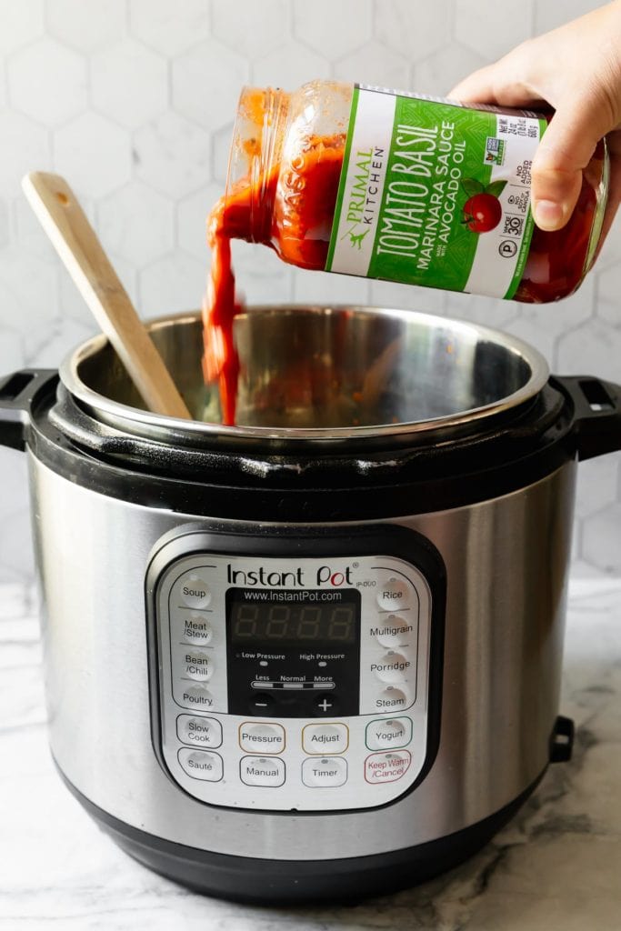 A jar of Primal Kitchen Tomato Basil Marinara Sauce being poured into an Instant Pot for homemade lasagna soup.