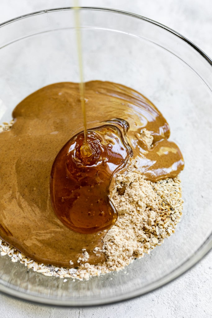 Honey being drizzled into a glass mixing bowl holding all ingredients for monster cookie peanut butter protein balls.
