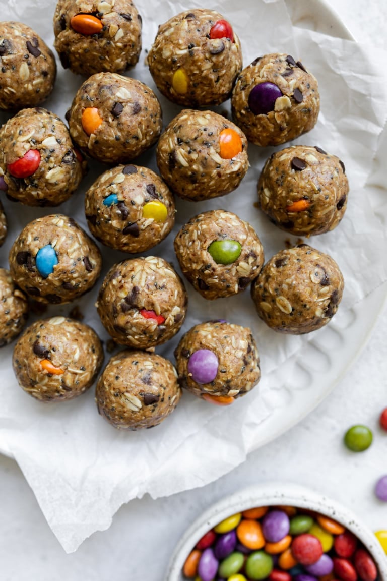 Overhead view of a plate of monster cookie protein balls and a dish of colorful chocolate coated candies on the side. 