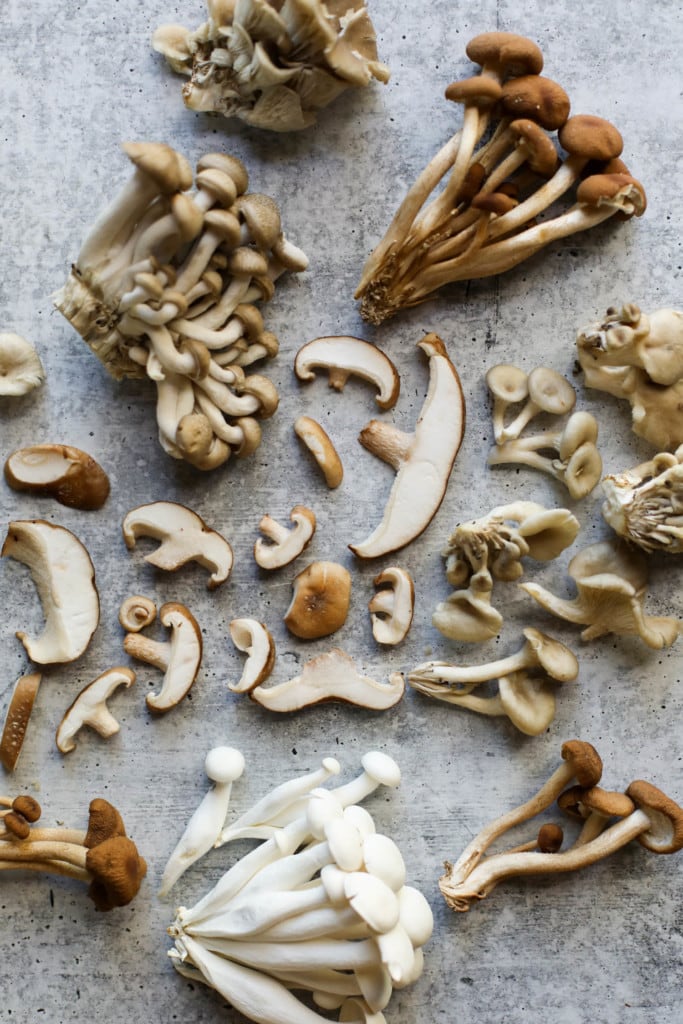 Overhead view of different varieties of mushrooms, cut and on a photo board.