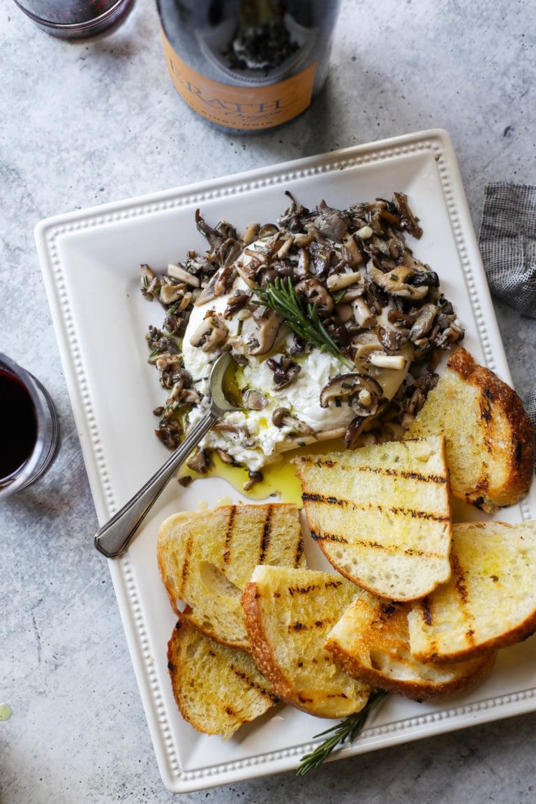 Overhead view of a plate filled with sauteed mushrooms over burrata, and a side of toasted sourdough topped with fresh olive oil drizzle.