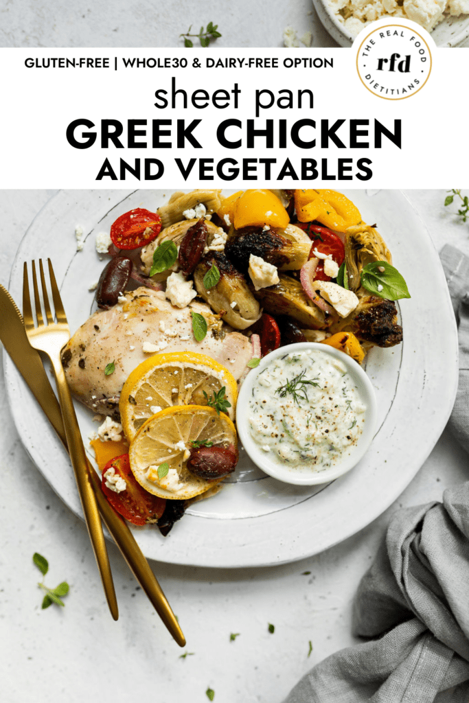 An overhead view of Sheep Pan Greek Chicken and Vegetables plated on a white plate topped with feta crumbles and a side of Tzatziki sauce.