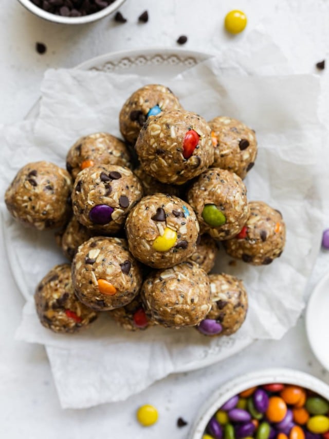 Pile of monster cookie protein balls with colorful candy-coated chocolate pieces on parchment-covered plate.