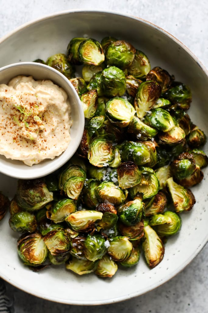 Overhead view of air fried Brussels sprouts on a platter with a small bowl of aioli on the side.