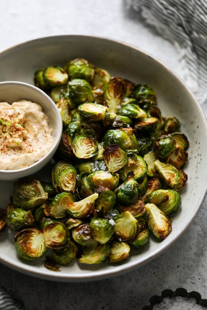 Air fryer Brussels sprouts plated on a tray next to a bowl of chipotle-lime aioli.