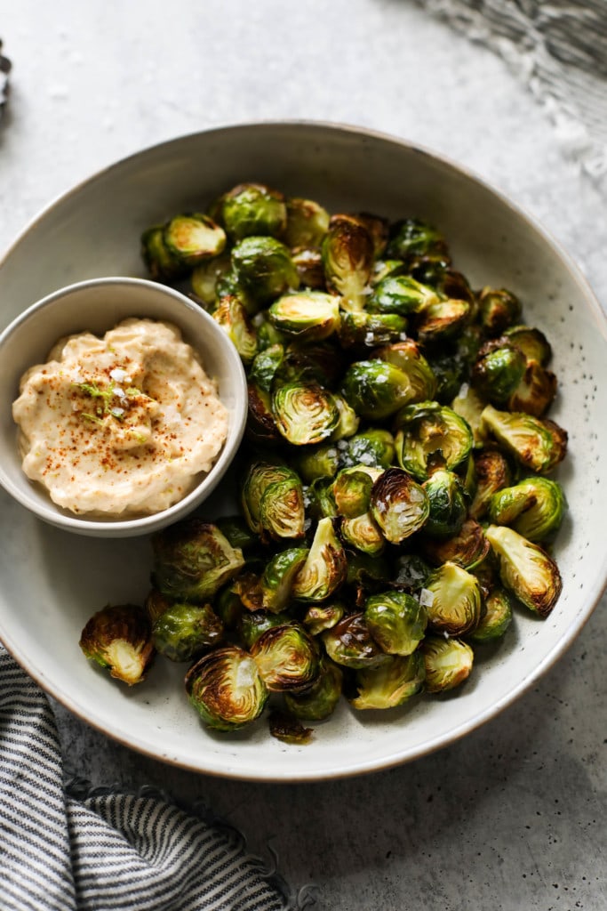 Overhead view of crispy roasted Brussels sprouts on a platter with a side bowl of aioli.
