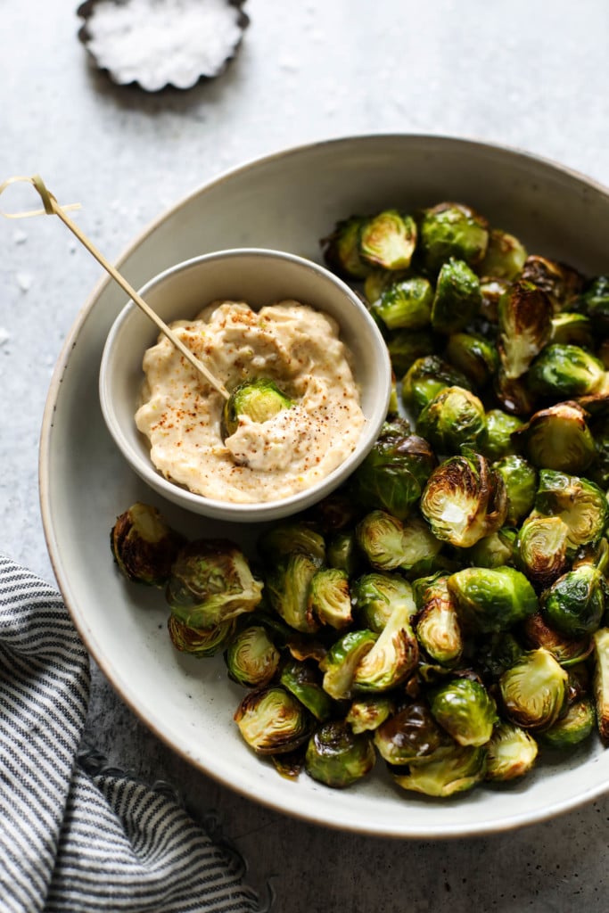 Roasted Brussels sprouts on a serving tray with chipotle aioli on the side. 