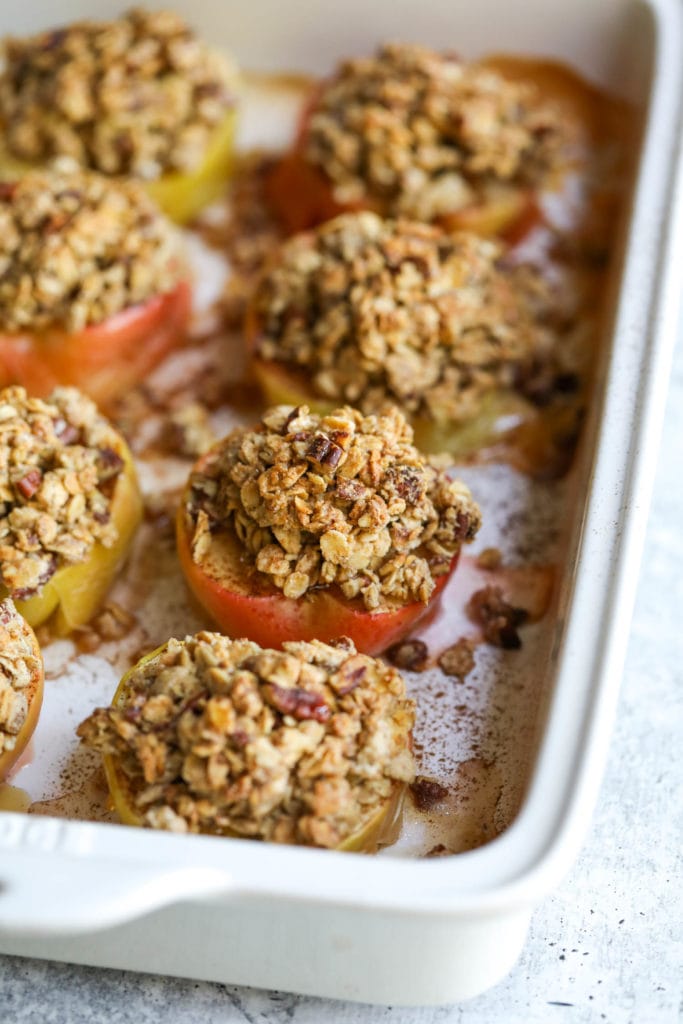 Close up view of baked apple halves topped with oat and pecan crumble in a white baking dish.