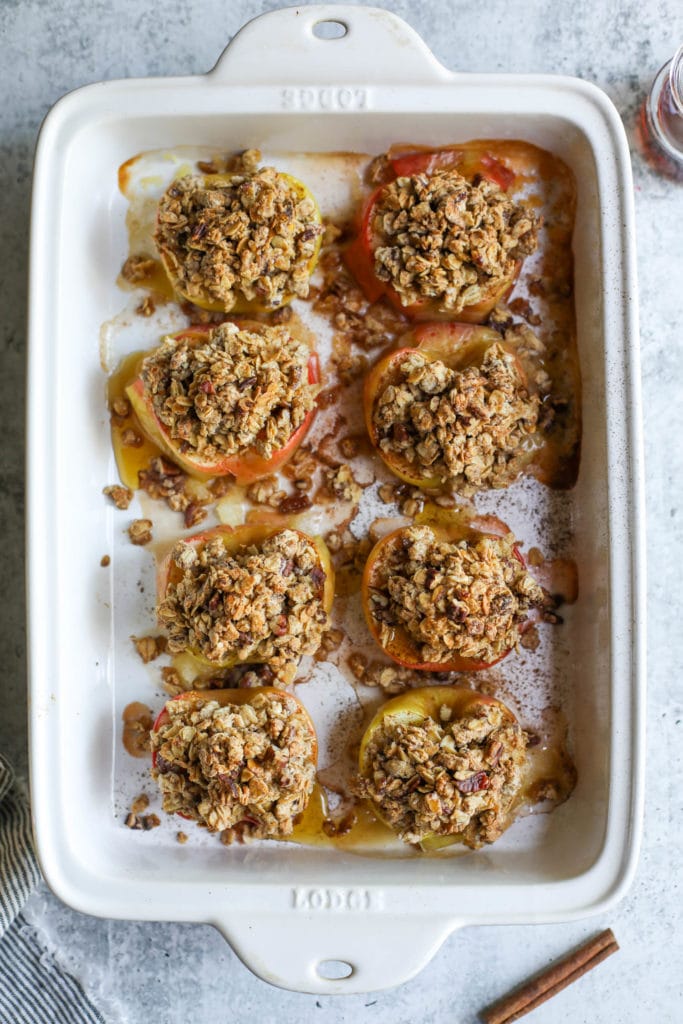 Eight apple halves topped with oat crumble in a white baking dish sprinkled with cinnamon.