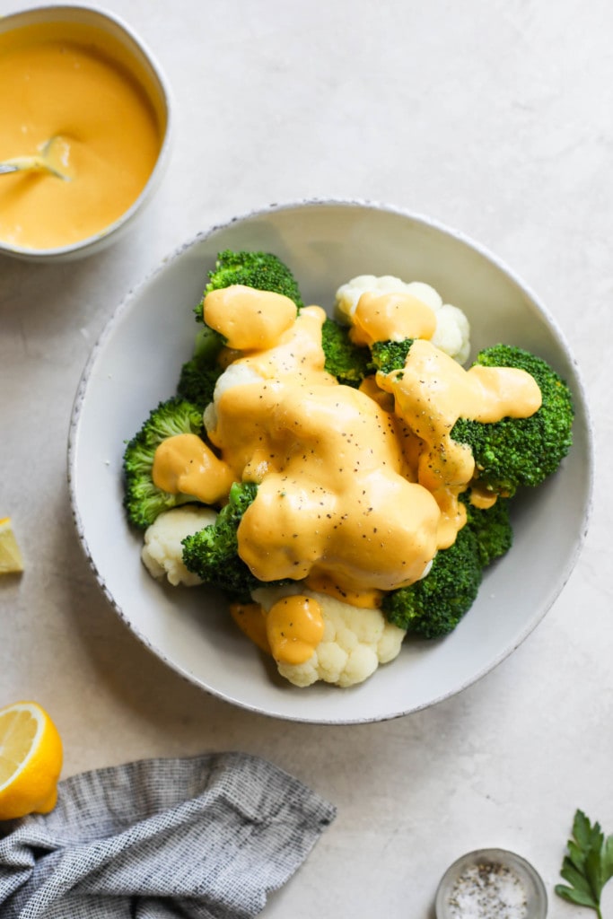 Overhead view of steamed cauliflower and broccoli in a bowl topped with vegan cheese sauce and cracked pepper.