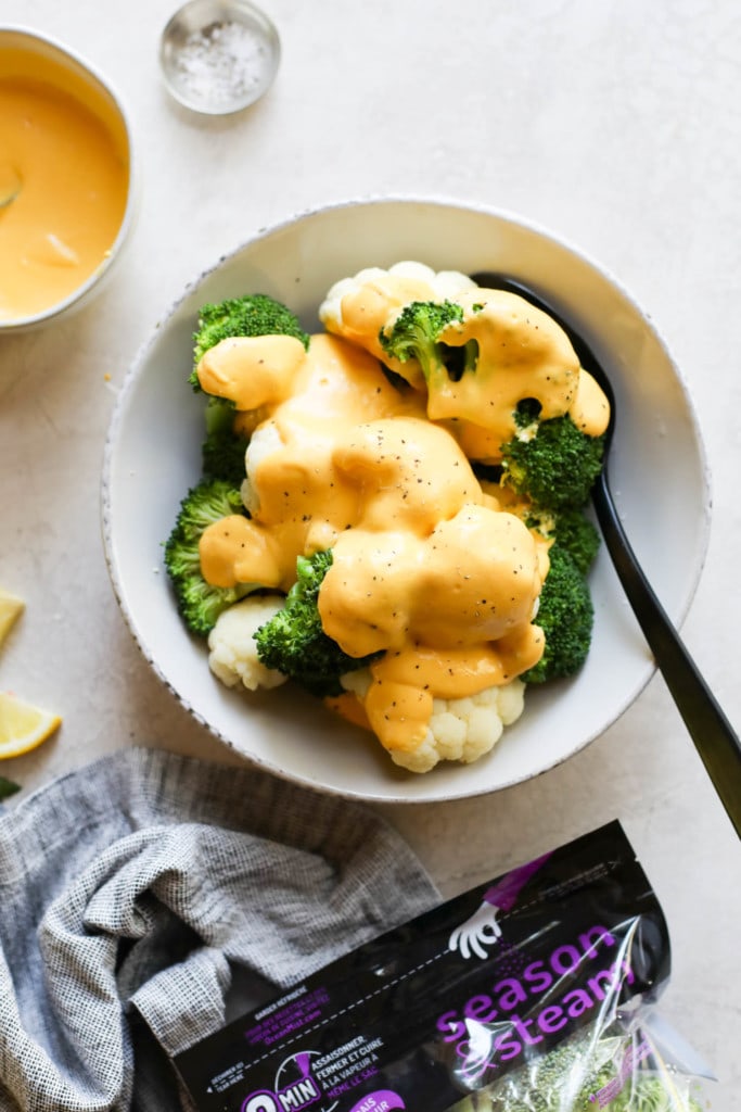 Vegan cheese sauce poured over a bowl filled with steamed broccoli and cauliflower.