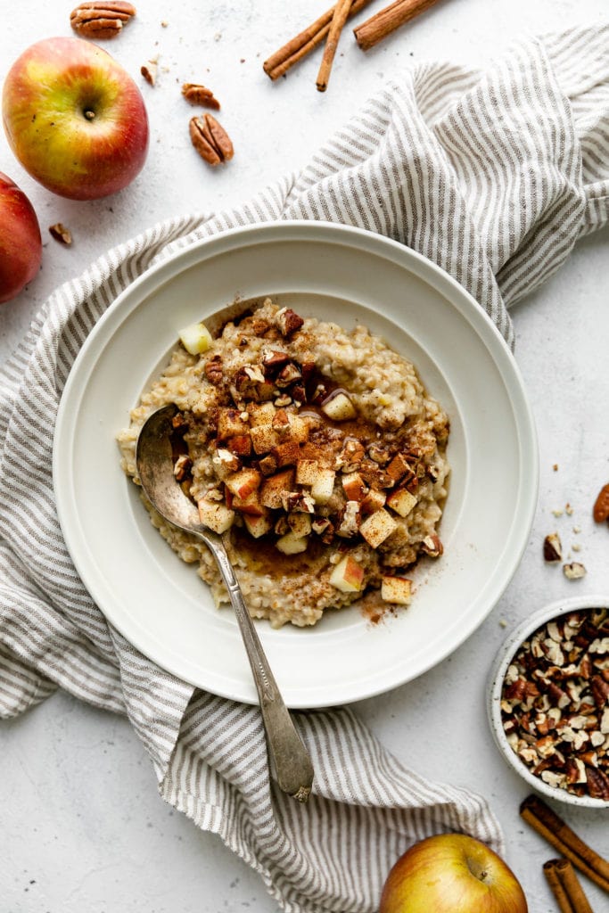 Overhead view of creamy Instant Pot steel cut oatmeal in a white bowl topped with apples and pecans. 