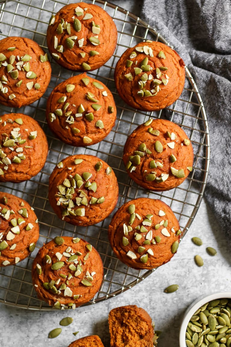 Close up view of pumpkin protein muffins cooling on a wire rack topped with pumpkin seed pieces. 