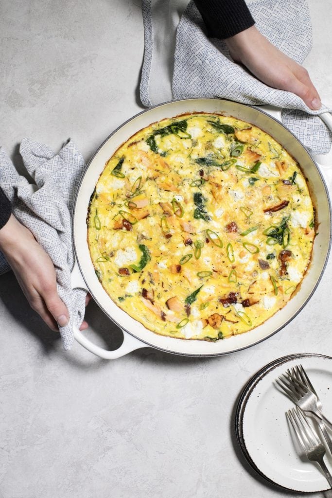 Two hands holding a white casserole dish with a frittata.