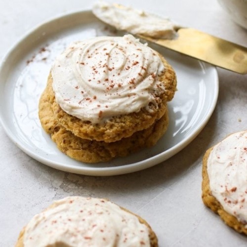 Two soft pumpkin cookies topped with cream cheese frosting on a white plate