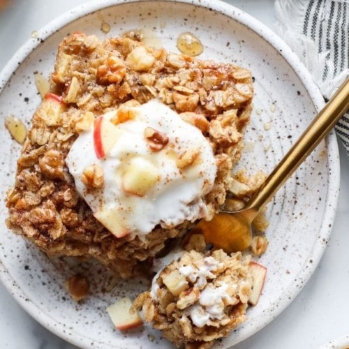 Apple cinnamon baked oatmeal on a plate topped with whipped cream.