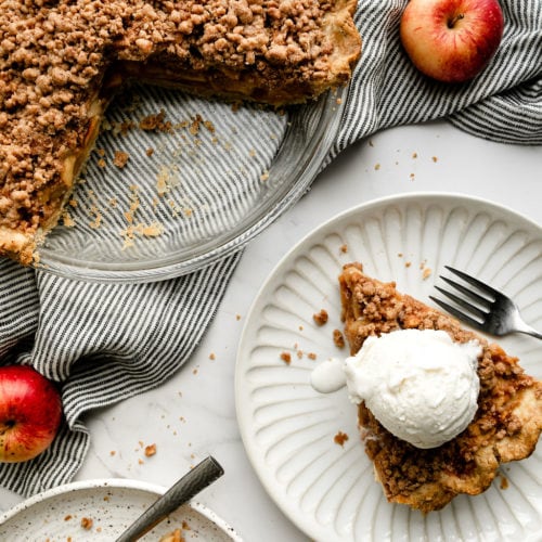 A slice of apple pie on a plate with a whole apple pie nearby for a Thanksgiving menu.
