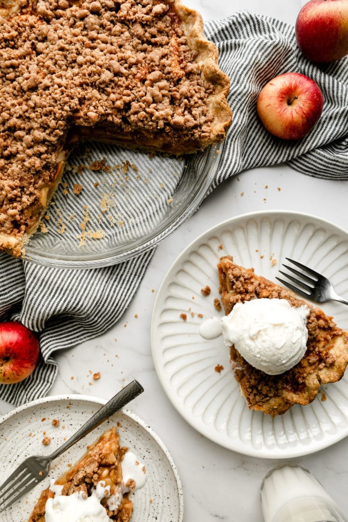 A slice of apple pie on a plate with a whole apple pie nearby for a Thanksgiving menu.