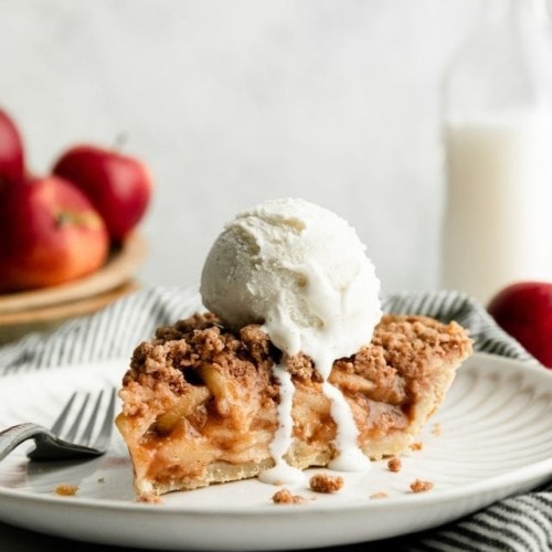A slice of gluten-free apple pie on a white plate with a scoop of melty ice cream on top.