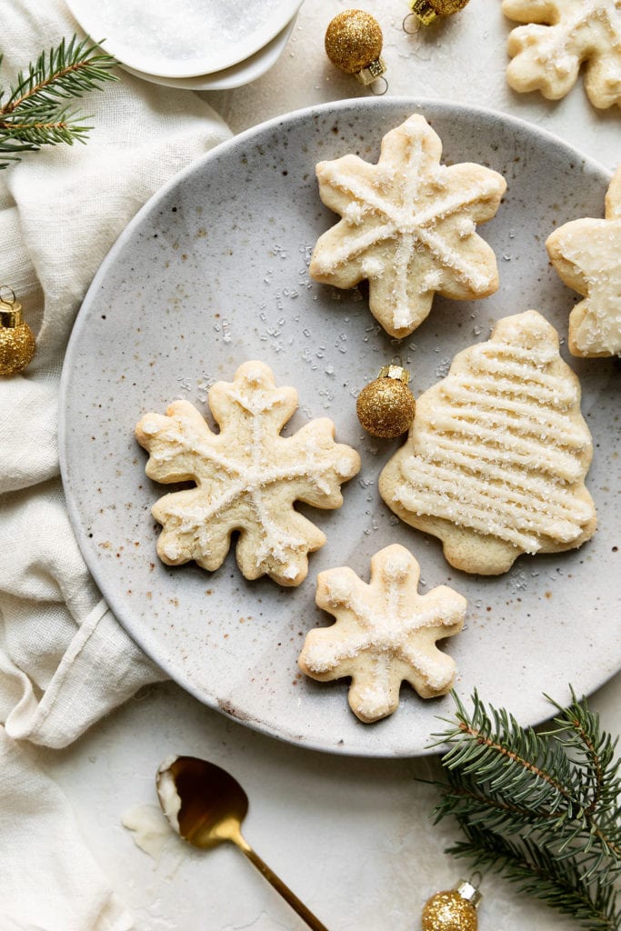 Several gluten-free cut-out cookies in Christmas trees, stars, and snowflakes with white piping on a speckled plate.