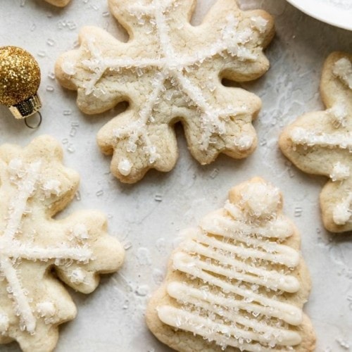 Gluten free sugar cookies cut out in snowflakes and Christmas trees with white frosting piped along edges.