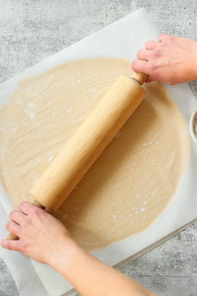 A rolling pin rolling out pie crust between two pieces of parchment paper.