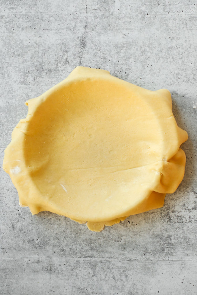 Gluten-free pie crust dough spread out over a pie plate with overhang