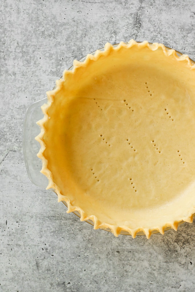 Close up view of gluten-free pie crust in a pie plate with fluted edges and fork marks in the bottom of the pie