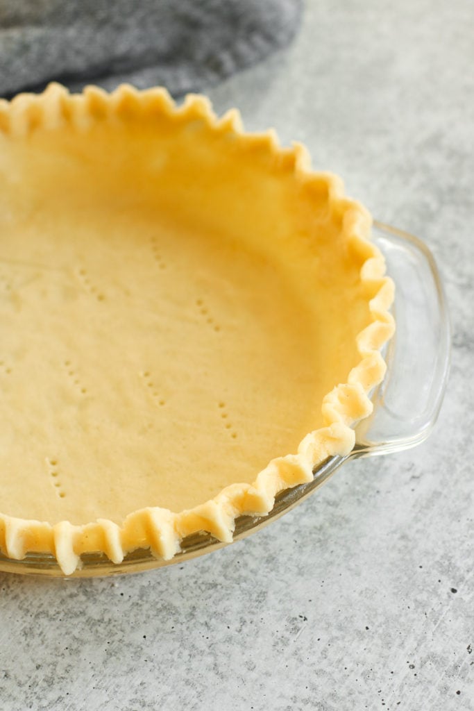 Gluten-free pie crust in a glass pie plate with fluted edges and fork marks in the bottom of the pie crust. 