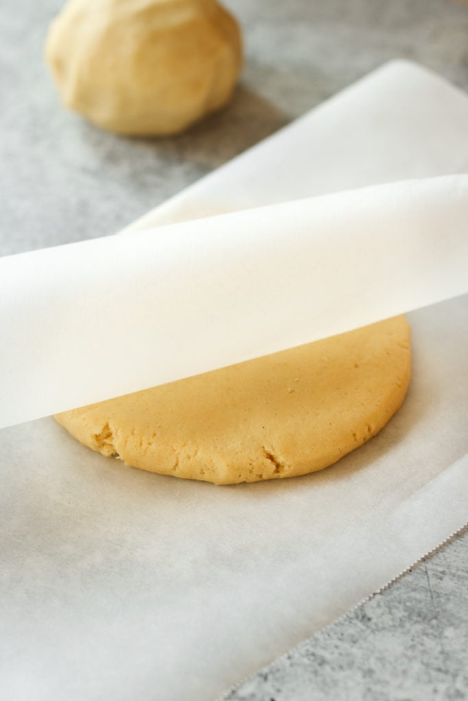 One pie crust dough ball flattened into a disc shape between parchment paper.