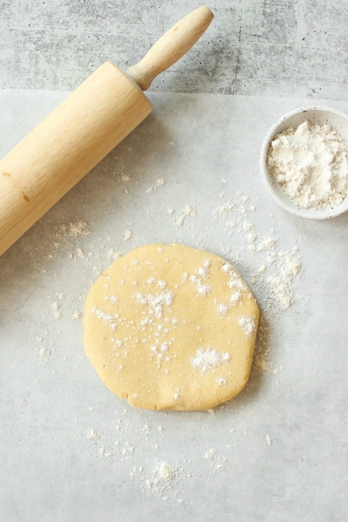 Gluten-free pie crust dough flattened to a disc on parchment paper sprinkled with flour