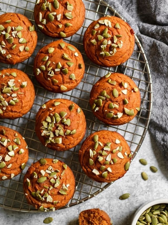 Overhead view of several freshly baked pumpkin protein muffins topped with pepitas on a cooling rack